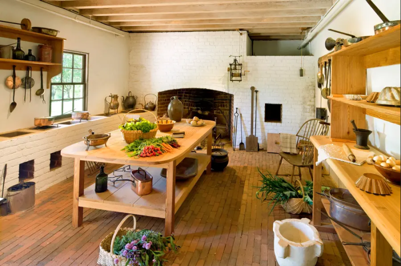 Monticello's replica 1809 kitchen with table in the middle shelves on right and stew stoves on left plus equipment and food items for display